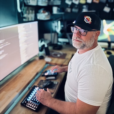 A photo of Cameron sitting at his desk, upon which is a single large external display.