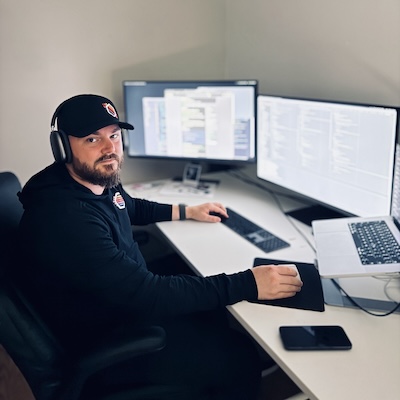 A photo of Sean sitting at his desk, upon which are an open notebook computer and two external displays.